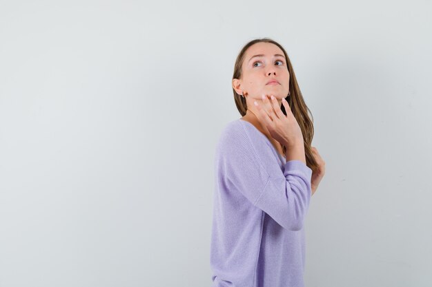 Junge Dame im Freizeithemd, die Hand am Kinn hält und zögernd schaut.