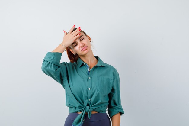 Junge Dame im grünen Hemd mit der Hand auf der Stirn und erschöpft, Vorderansicht.