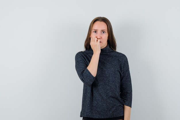 Junge Dame im Hemd beißt Nägel emotional und sieht ängstlich aus