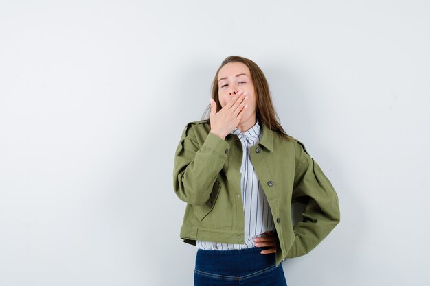 Junge Dame im Hemd, Jacke, die Hand auf den Mund hält, während sie gähnt und schläfrig aussieht, Vorderansicht.