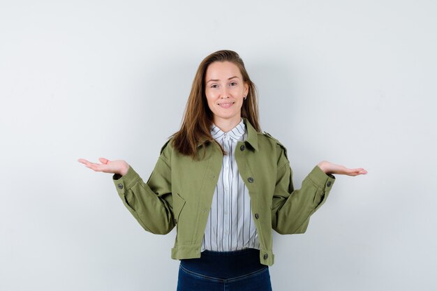 Junge Dame im Hemd, Jacke, die Skalengeste macht und fröhlich aussieht, Vorderansicht.