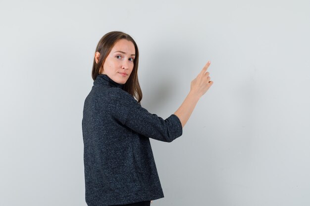 Junge Dame im Hemd zeigt nach oben, während sie nach vorne schaut und vernünftige Rückansicht schaut