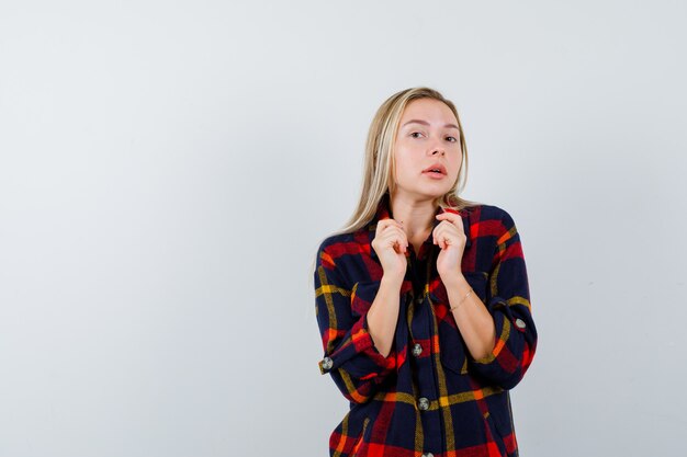 Junge Dame im karierten Hemd, das Kragen des Hemdes hält und selbstbewusst, Vorderansicht schaut.