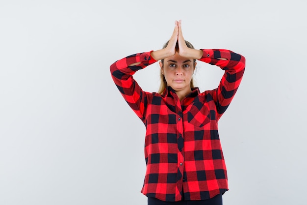 Kostenloses Foto junge dame im karierten hemd, das namaste geste zeigt und selbstbewusst aussieht