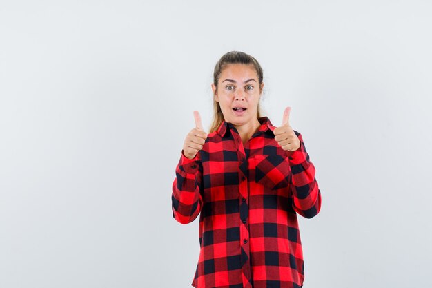 Junge Dame im karierten Hemd, die doppelte Daumen hoch zeigt und erstaunt schaut