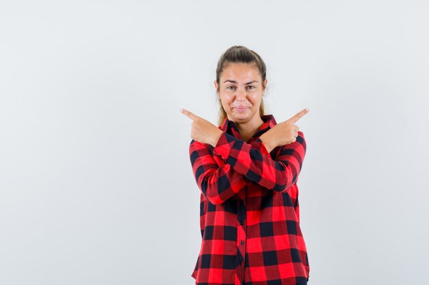 Junge Dame im karierten Hemd zeigt weg und sieht selbstbewusst aus