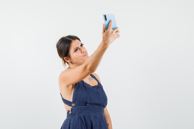 Junge Dame im Kleid macht Selfie auf dem Handy und sieht hübsch aus