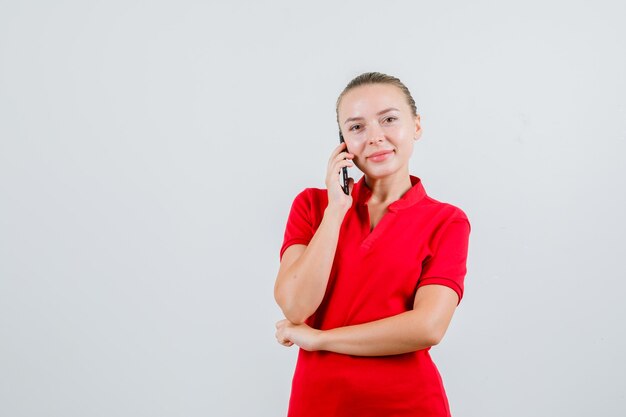 Junge Dame im roten T-Shirt, das auf Handy spricht und fröhlich schaut