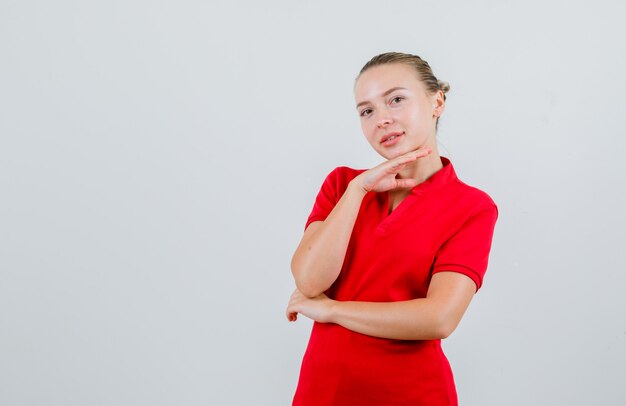 Junge Dame im roten T-Shirt, das Kinn auf Hand stützt und fröhlich schaut