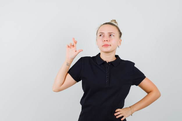 Junge Dame im schwarzen T-Shirt, das Daumen drückt und nachdenklich aussieht