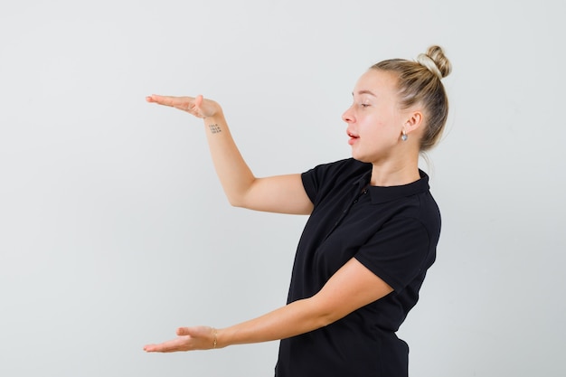 Junge Dame im schwarzen T-Shirt, das großes Zeichen zeigt und konzentriert schaut