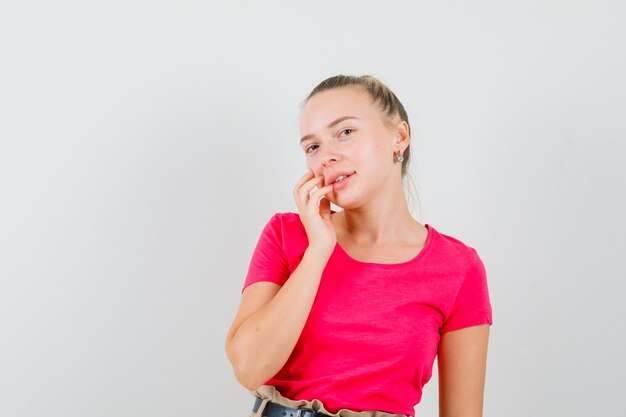 Junge Dame im T-Shirt, das ihre Gesichtshaut berührt und elegant aussieht