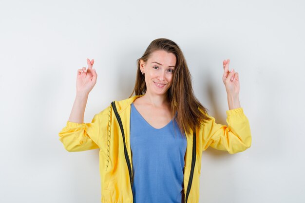 Junge Dame im T-Shirt, die die Daumen drückt und hoffnungsvoll aussieht, Vorderansicht.