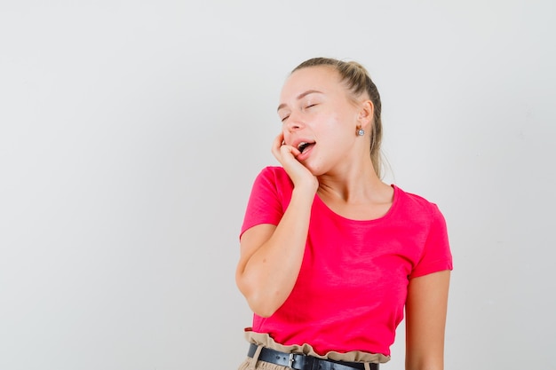 Junge Dame im T-Shirt, die ihre Gesichtshaut berührt und zart aussieht