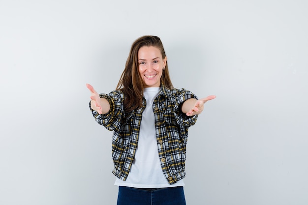 Junge Dame im T-Shirt, in der Jacke, in den Jeans, die Geste zeigen und freudig schauen, Vorderansicht.