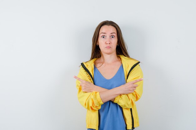 Junge Dame im T-Shirt, Jacke, die auf beide Seiten zeigt und zögerlich aussieht, Vorderansicht.