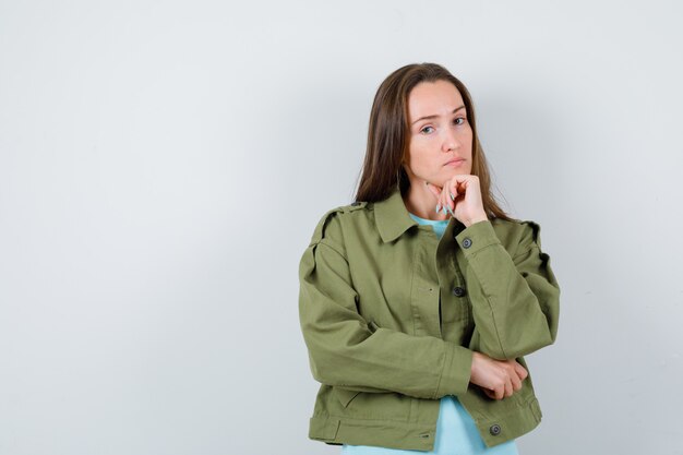 Junge Dame im T-Shirt, Jacke, die das Kinn auf die Faust stützt und selbstbewusst aussieht, Vorderansicht.