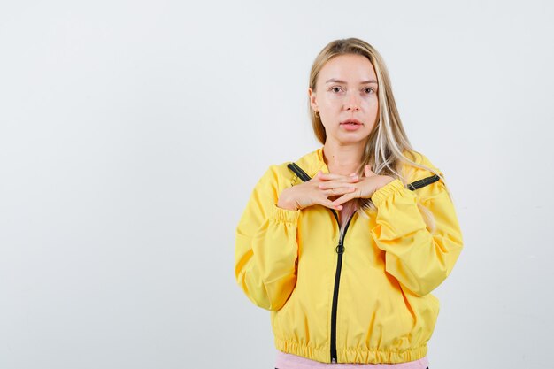 Junge Dame im T-Shirt, Jacke, die Hände auf Brust hält und selbstbewusst aussieht