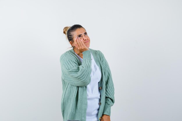 Junge Dame im T-Shirt, Jacke, die Hand auf Wange hält und nachdenklich aussieht