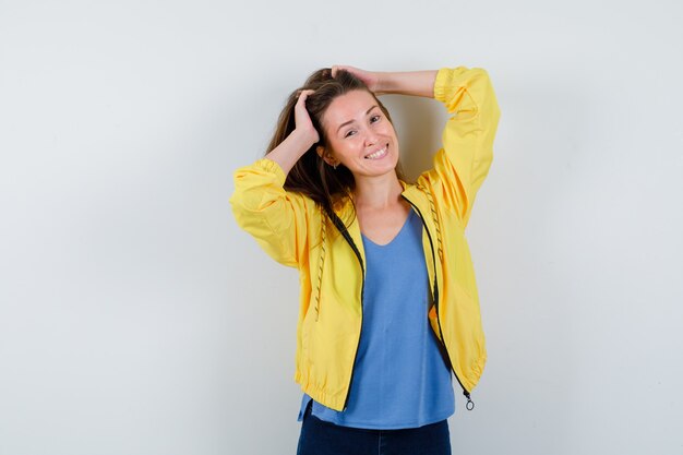 Junge Dame im T-Shirt, Jacke posiert, während sie die Hände auf dem Kopf hält und schwindlig aussieht, Vorderansicht.