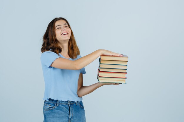 Junge Dame im T-Shirt, Jeans, die Bücher halten und Kirsche schauen, Vorderansicht.