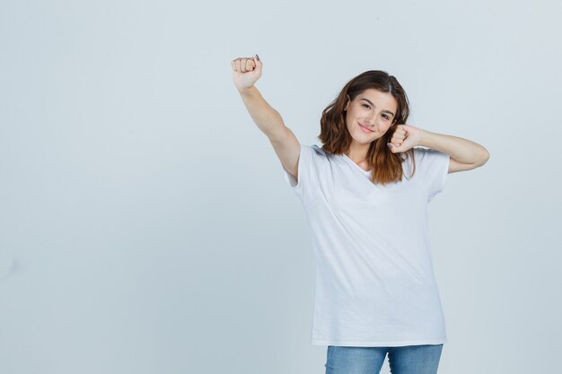 Junge Dame im T-Shirt, Jeans, die Siegergeste zeigt und glücklich schaut, Vorderansicht.