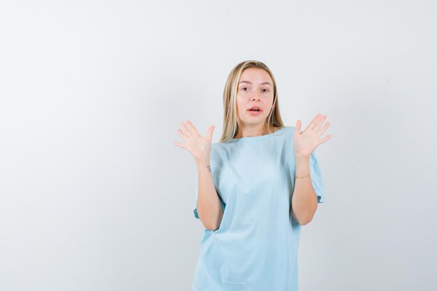 Junge Dame im T-Shirt mit Handflächen in Kapitulationsgeste und verwirrt isoliert