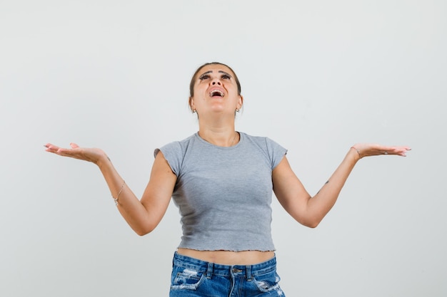 Junge Dame im T-Shirt, Shorts, die aufblicken, Hände ausbreiten und hoffnungsvoll aussehen