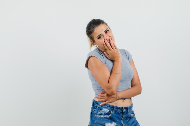 Junge Dame im T-Shirt, Shorts, die Hand auf Mund halten