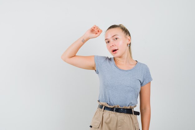 Junge Dame im T-Shirt und in der Hose, die beim Anheben des Armes aufwirft und elegant aussieht