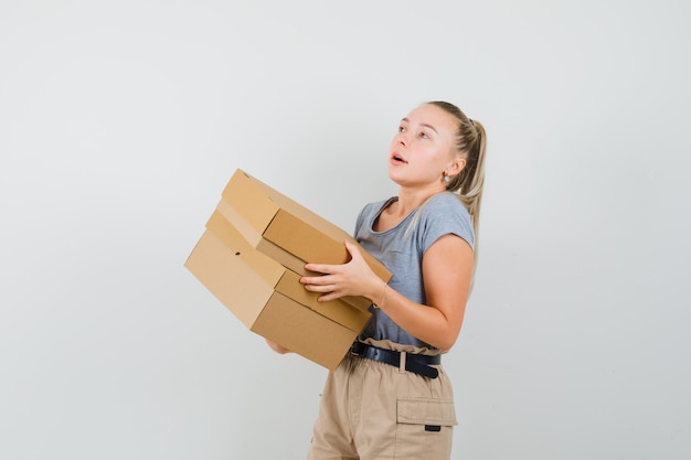 Junge Dame im T-Shirt und in der Hose, die Pappkartons halten und überrascht, Vorderansicht schauen