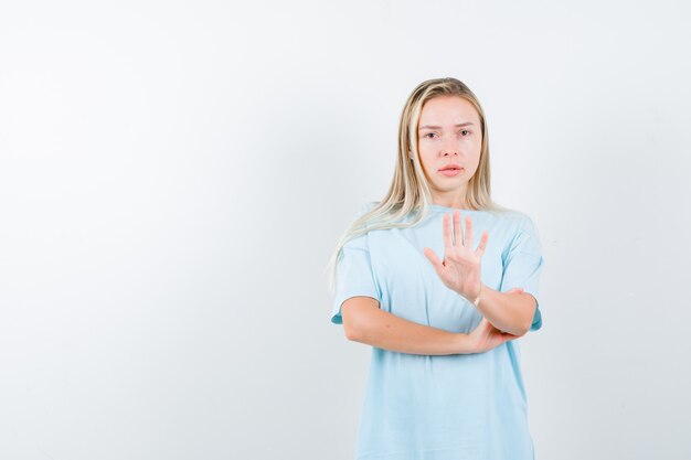 Junge Dame im T-Shirt zeigt Stoppgeste und schaut selbstbewusst, Vorderansicht.