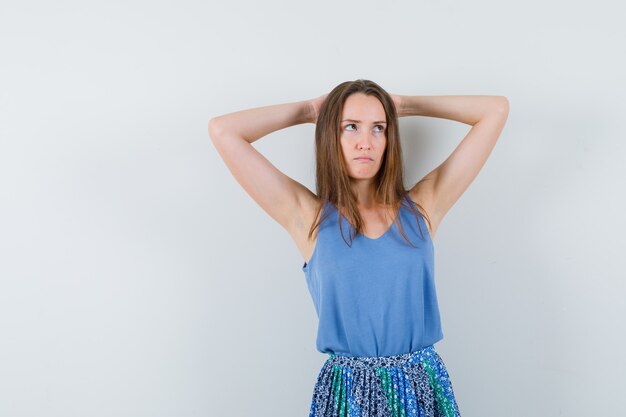 Junge Dame im Unterhemd, Rock, der Hände hinter Kopf hält und zögernd, Vorderansicht schaut.