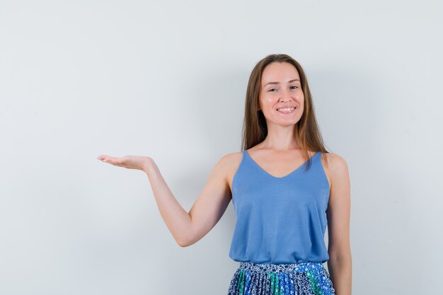 Junge Dame im Unterhemd, Rock, der Handfläche beiseite spreizt und fröhlich schaut, Vorderansicht.