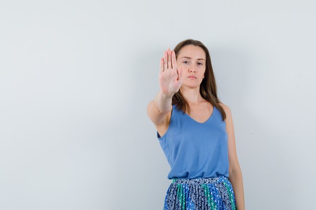 Junge Dame im Unterhemd, Rock zeigt Stoppgeste und sieht ernst aus