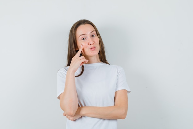 Junge Dame im weißen T-Shirt, das Finger auf Wange hält und verträumt aussieht