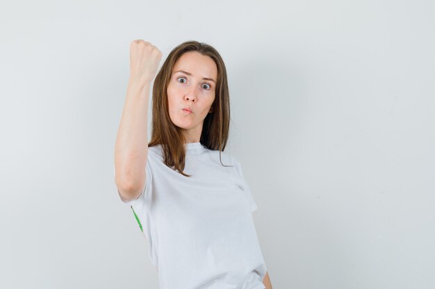 Junge Dame im weißen T-Shirt, das geballte Faust zeigt und mächtig aussieht