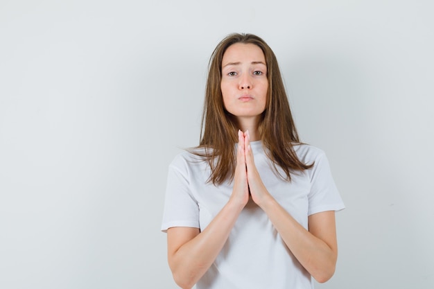 Junge Dame im weißen T-Shirt, das Hände in der Gebetsgeste hält und hoffnungsvoll aussieht