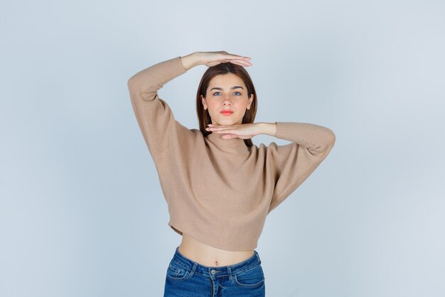 Junge Dame in beigem Pullover, Jeans mit Größenschild und selbstbewusstem Blick, Vorderansicht.