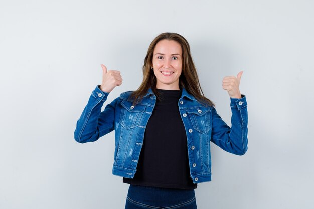 Junge Dame in Bluse, die doppelte Daumen nach oben zeigt und selbstbewusst aussieht, Vorderansicht.