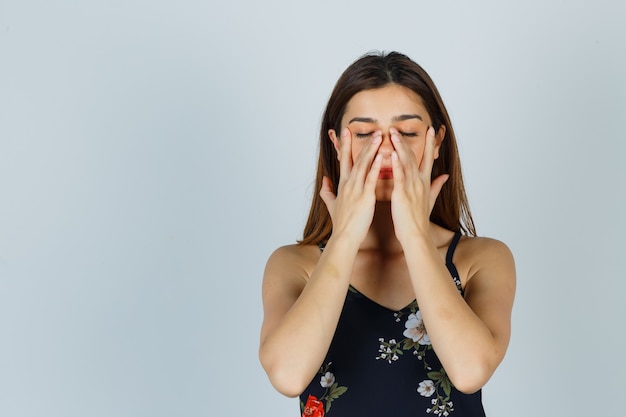 Junge Dame in Bluse, die vorgibt, Gesichtsmaske um die Nasenzone herum zu reiben und entspannt auszusehen, Vorderansicht.