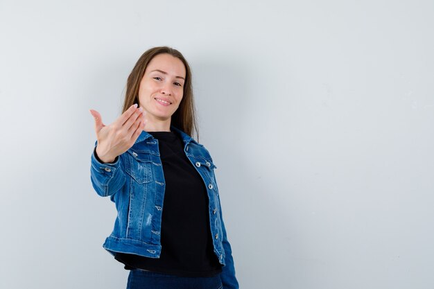 Junge Dame in Bluse, Jacke, die zum Kommen einlädt und fröhlich aussieht, Vorderansicht.