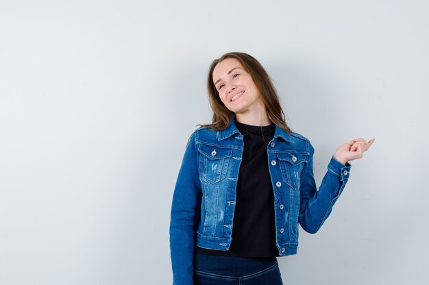 Junge Dame in Bluse, Jacke zur Seite zeigend und fröhlich aussehend, Vorderansicht.