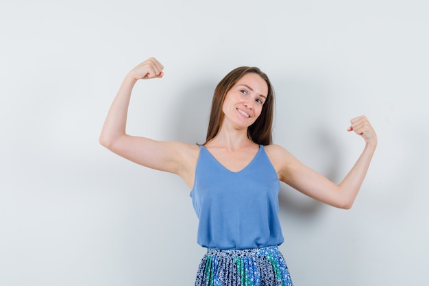 Junge Dame in Bluse, Rock zeigt ihre Armmuskeln und schaut energisch, Vorderansicht.