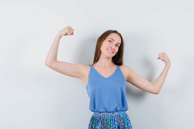 Junge Dame in Bluse, Rock zeigt ihre Armmuskeln und schaut energisch, Vorderansicht.