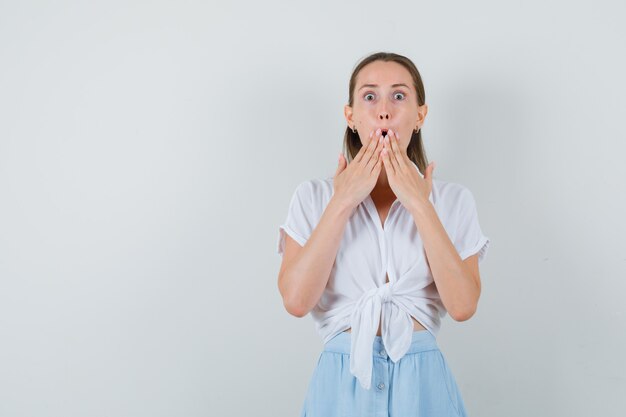 Junge Dame in Bluse und Rock hält Hände am Mund und sieht verwundert aus