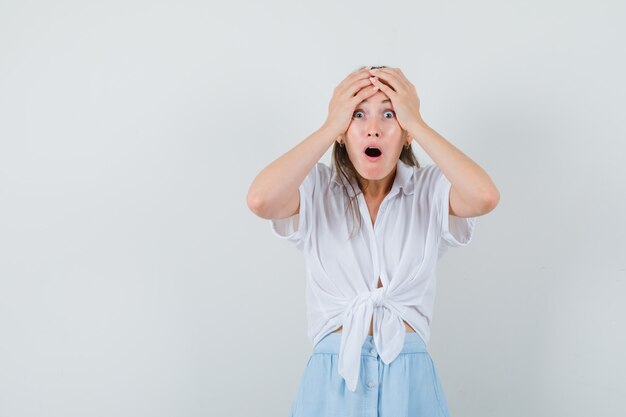 Junge Dame in Bluse und Rock Händchen haltend auf dem Kopf und wehmütig aussehend