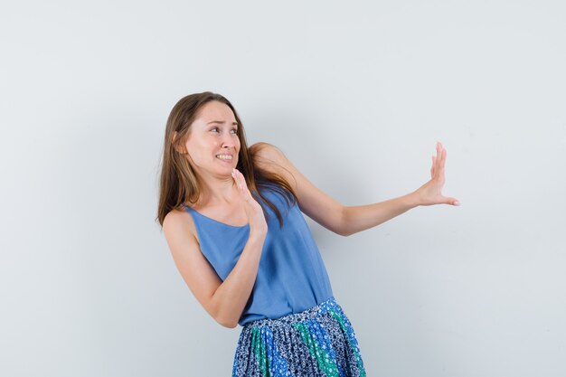 Junge Dame in der blauen Bluse, Rock, der Hände zum Verteidigen anhebt und angewidert aussieht, Vorderansicht.