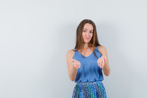 Junge Dame in der blauen Bluse, Rock, der offene Handflächen anhebt, während sie etwas vor der Kamera zeigt, Vorderansicht.