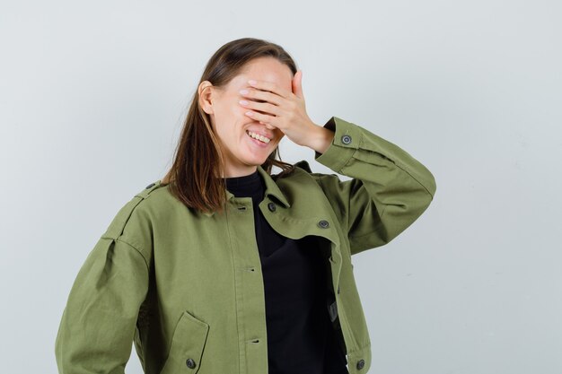 Junge Dame in der grünen Jacke, die Hand auf Augen hält und aufgeregt, Vorderansicht schaut.